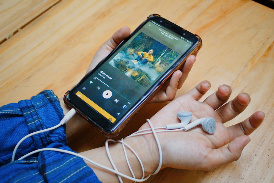 A person holding a cell phone with ear buds in their hands